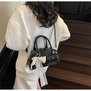 Detail of black glossy Boston bag with lace pearl bow charm worn by a model