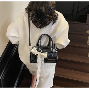 Black patent leather Boston bag with white lace bow and pearls shown on a model