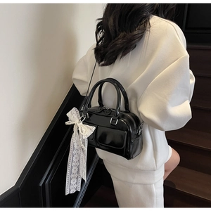 Detail of black patent leather Boston bag with white lace bow pearl charm on model