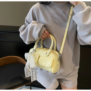 Detail of pale yellow patent leather Boston bag with decorative pearl lace bow pendant