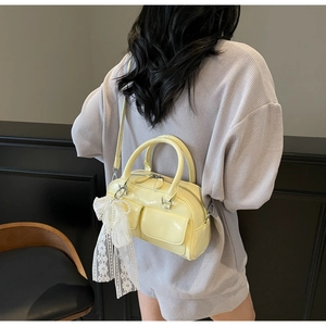 Detail of light yellow patent leather Boston bag featuring lace bow and dual pockets
