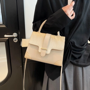 Cream crossbody bag with crocodile texture and gold buckle shown on a pedestal