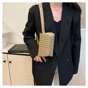 Détail du sac bandoulière punk beige à rivets argentés porté sur un blazer noir
