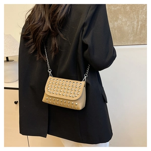 Détail du sac bandoulière punk beige avec clous argentés et chaîne porté par un modèle