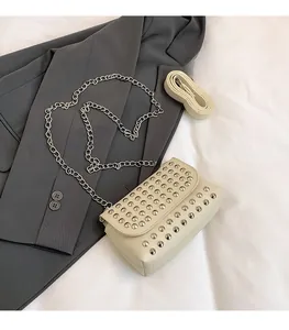 Détail du sac à rabat blanc cassé avec rivets argentés et chaîne en métal sur un blazer