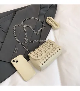 Détail du petit sac beige à rivets avec chaînes argentées sur un blazer gris