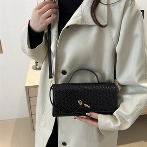 Sac baguette en cuir tressé noir avec fermoir doré sur un trench-coat de couleur beige