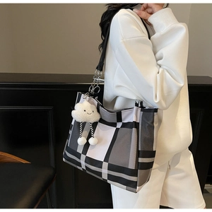 Detail of checkered tote bag featuring a cute white plush cloud charm on the side strap