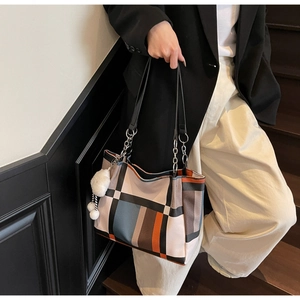 Detail of color-block tote bag with silver chain strap and plush ball on a model