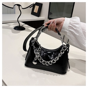 Détail du sac sous l'aisselle en cuir verni noir avec grosse chaîne argentée et lanière