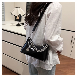 Détail du sac bandoulière noir verni avec chaîne argentée et pendentif métallique