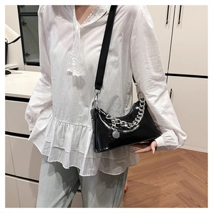 Vue détaillée du sac bandoulière noir brillant avec chaîne argentée et pendentif en métal