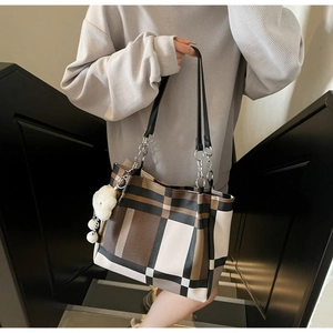 Detail of checkered tote bag with leather straps, metal chains and a plush bear charm
