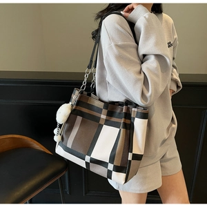 Detail view of large checkered tote bag with metal chain strap and white pom-pom charm