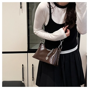 Détail d'un sac à main marron café brillant avec chaîne argentée et pendentif rond