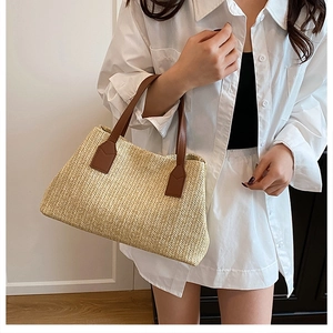 Detail of V-shaped woven straw tote bag with brown leather handles and reinforced stitching