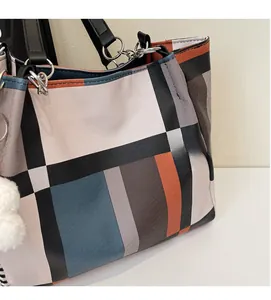 Close-up of contrast checkered tote bag with leather handle and white pom-pom charm