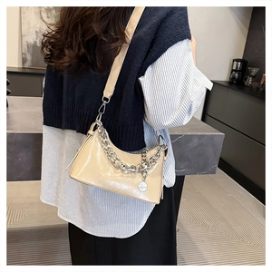 Détail du sac en cuir verni beige avec chaîne argentée et pendentif porté par un mannequin