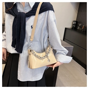 Gros plan d'un sac à bandoulière beige en cuir ciré avec chaîne argentée et pendentif