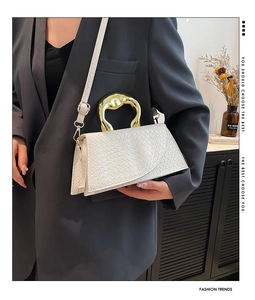 Detail of white textured leather bag with sculptural gold handle on a grey suit model