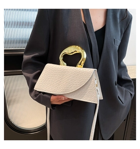 Detail of white crocodile pattern bag with unique gold metal ring handle and asymmetric shape