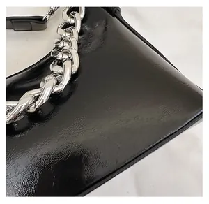 Gros plan sur la texture en cuir ciré noir brillant et la chaîne argentée du sac à main