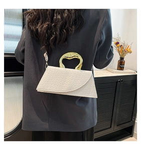 Close-up of a white textured handbag featuring a unique golden metallic curved handle