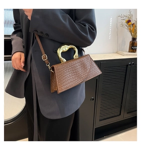 Detail of woven brown leather bag featuring a unique heart-shaped gold metal handle