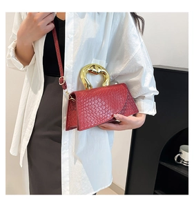 Detail of burgundy textured leather bag with unique sculptural gold metal handle