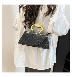 Detail of black crocodile texture handbag featuring a unique gold metal handle and strap