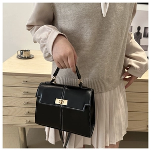 Detail of black contrast stitch handbag with gold twist lock held in a lifestyle setting