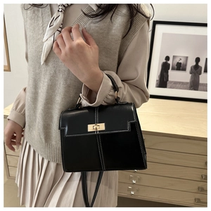 Model showcasing a black leather Kelly handbag with white contrast stitching and gold lock