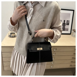 Detail showing the black leather crossbody bag with white contrast stitching and gold lock