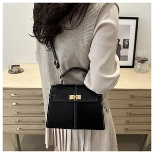 Detail of black leather handbag with white contrast stitching and gold metal twist lock