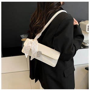 Detail showing creamy white glossy baguette bag with rhinestone buckle and silk scarf strap