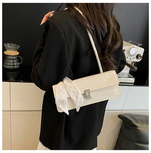 Detail view of a cream shoulder bag featuring a diamond buckle and heart-patterned silk scarf