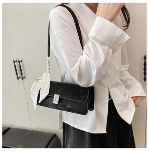 Detail of black suede underarm bag featuring a silver metal buckle and silk scarf accent
