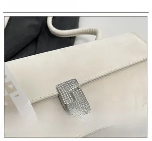 Close-up of bejeweled L-shaped metal lock and suede texture on beige shoulder bag