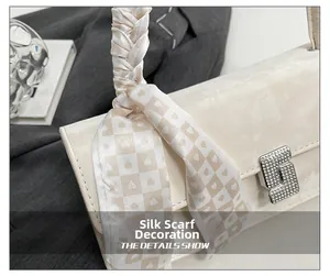 Detail of cream shoulder bag featuring silk scarf handle and silver metal turn-lock