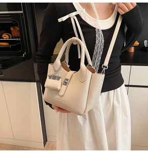 Detail van beige tas met litchi-textuur leer, metalen slot en mini-accessoire