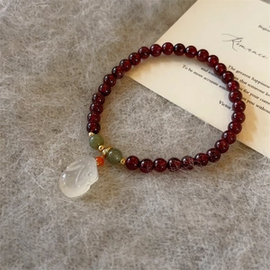 Dettaglio del bracciale di granato con ciondolo a coniglio in giada bianca su peluche