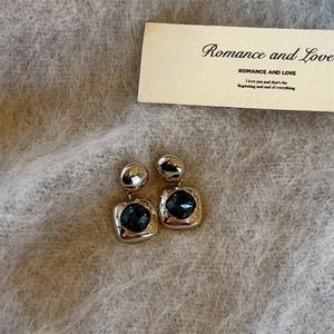 Detailed close-up of vintage gold square earrings with blue gems on grey plush fabric