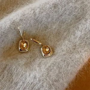 Detailed macro of small square diamond earrings with amber crystal and gold finish
