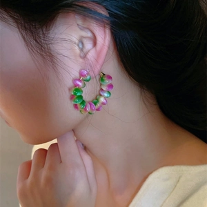 Close-up of model wearing large hoop earrings with pink and green gradient cat-eye beads