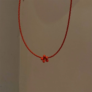 Macro shot of handmade red beaded necklace featuring a delicate yellow and red daisy charm