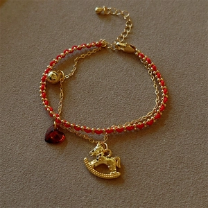 Detail of red woven cord bracelet with gold beads, rocking horse, and heart charms