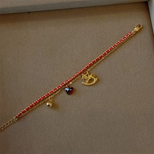 Close-up of double-layer bracelet with red rope, gold chain and rocking horse pendant