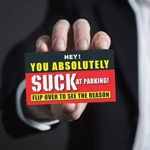 Close-up of hand holding a funny 'You Suck at Parking' card with bold warning text