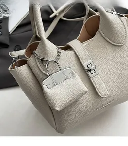 Detail van gebroken witte handtas met litchi-textuur, zilveren draaislot en hanger