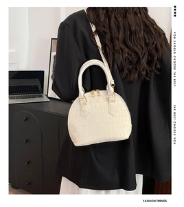 Detalle de bolso blanco con textura de cocodrilo, cremallera metálica y asas redondas